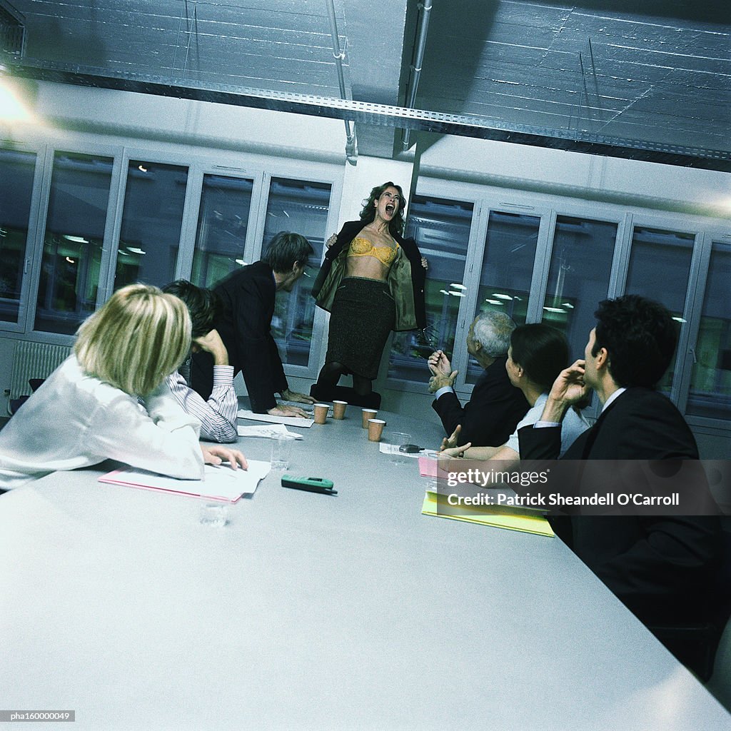 Young woman office worker standing on chair, stripping, colleagues watching.