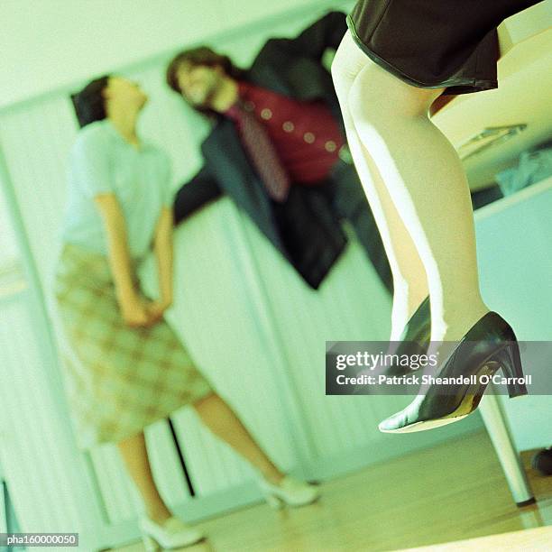 woman sitting on table, couple in background playing around, focus on sitting woman's legs. - carroll stock pictures, royalty-free photos & images