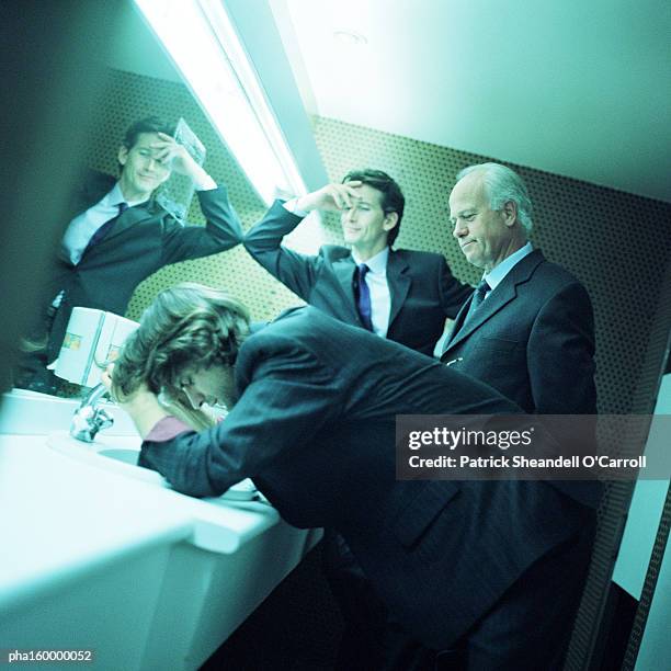 three businessmen in bathroom, two with hands on head, side view. - o foto e immagini stock