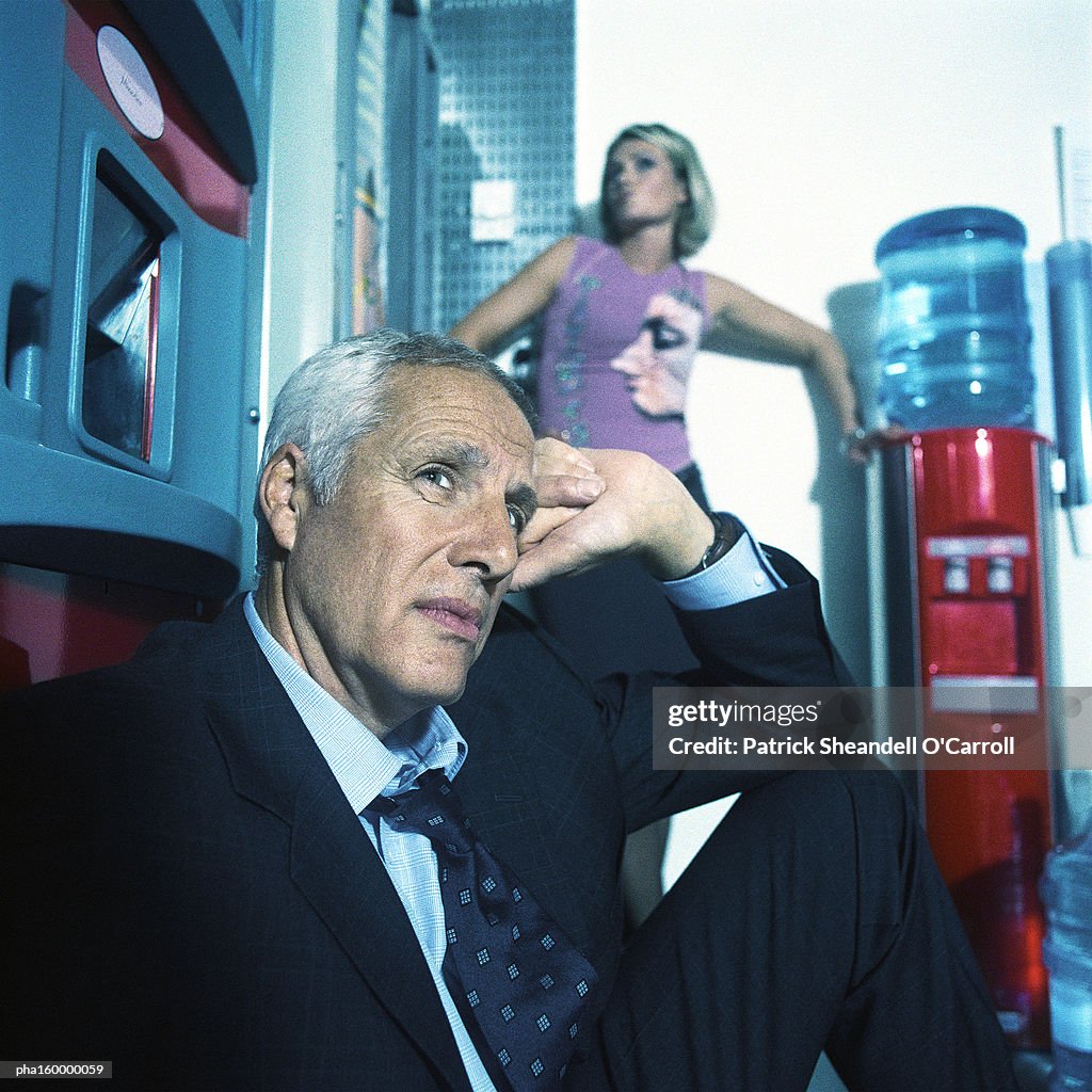 Mature businessman sitting in chair, young woman behind posing.