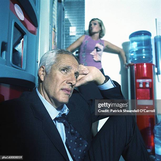 mature businessman sitting in chair, young woman behind posing. - man leaning chair standing side view stock pictures, royalty-free photos & images