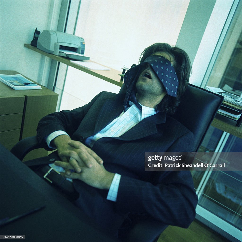 Young businessman sleeping at desk, tie covering eyes.