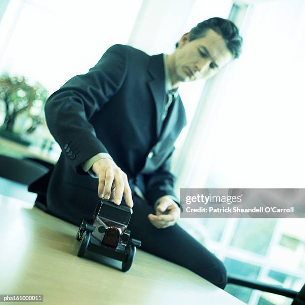 man sitting on desk, hand on old-fashioned model car, tilt. - carroll stock pictures, royalty-free photos & images