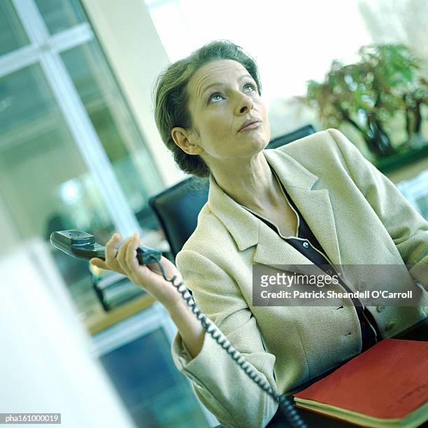 woman seated, holding phone away, looking up. - carroll stock pictures, royalty-free photos & images