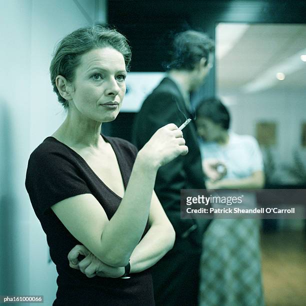 woman smoking, arms crossed, people in background. - o foto e immagini stock