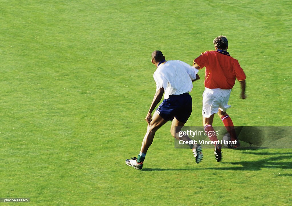 Two soccer players running for ball, full length