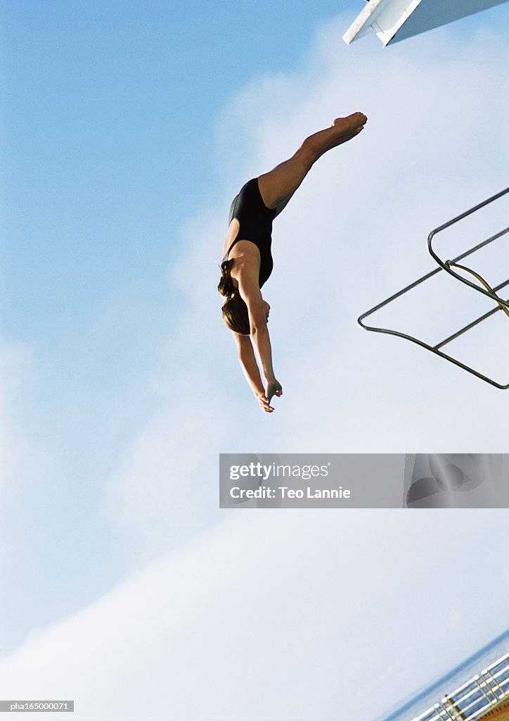 Woman in mid-dive, low angle view, full length, blue sky in background.
