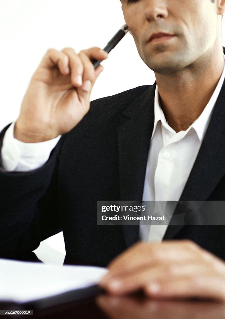 Businessman at desk, holding pencil, close-up