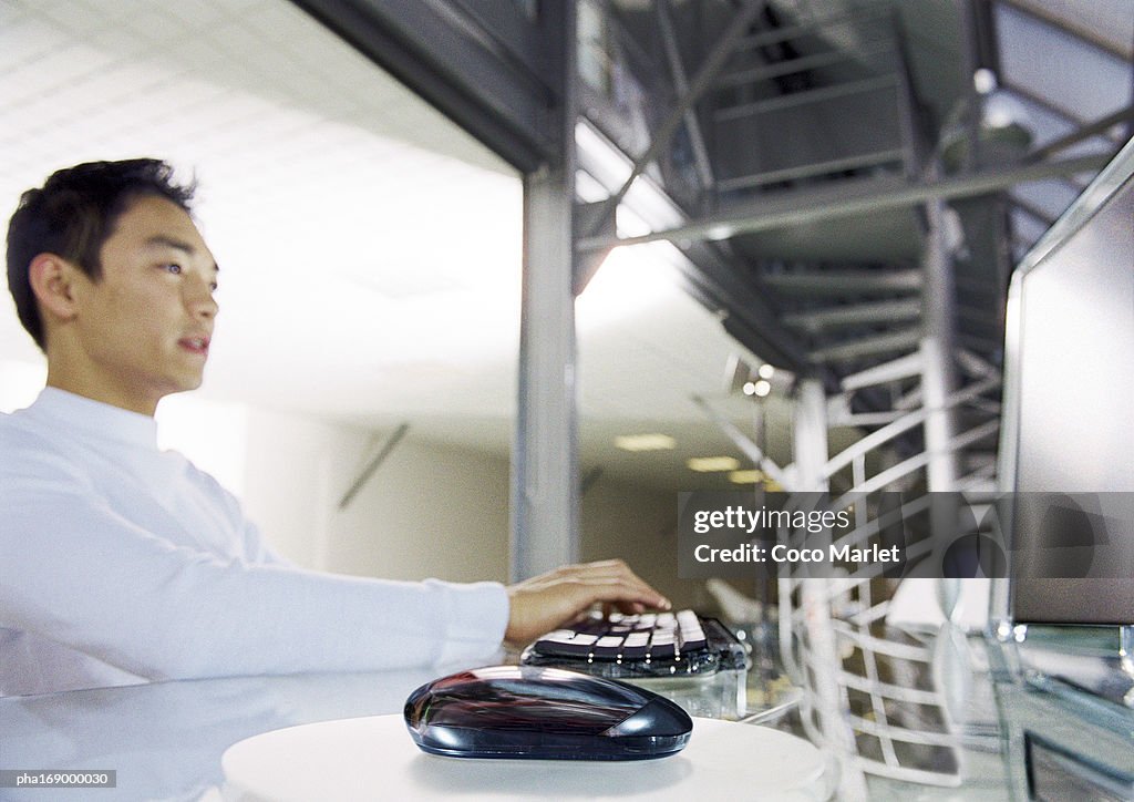 Man working on computer, side view, focus on mouse in foreground