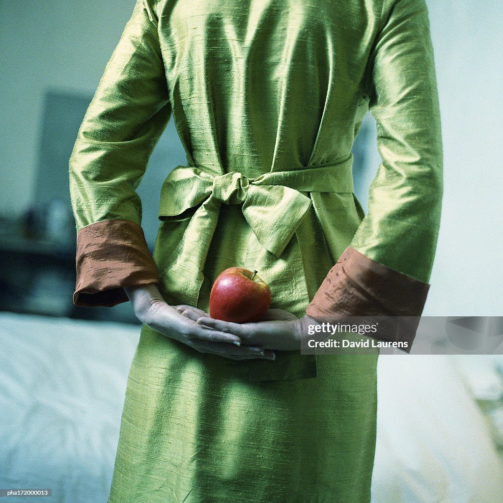 Woman holding apple behind back, mid-section, rear view