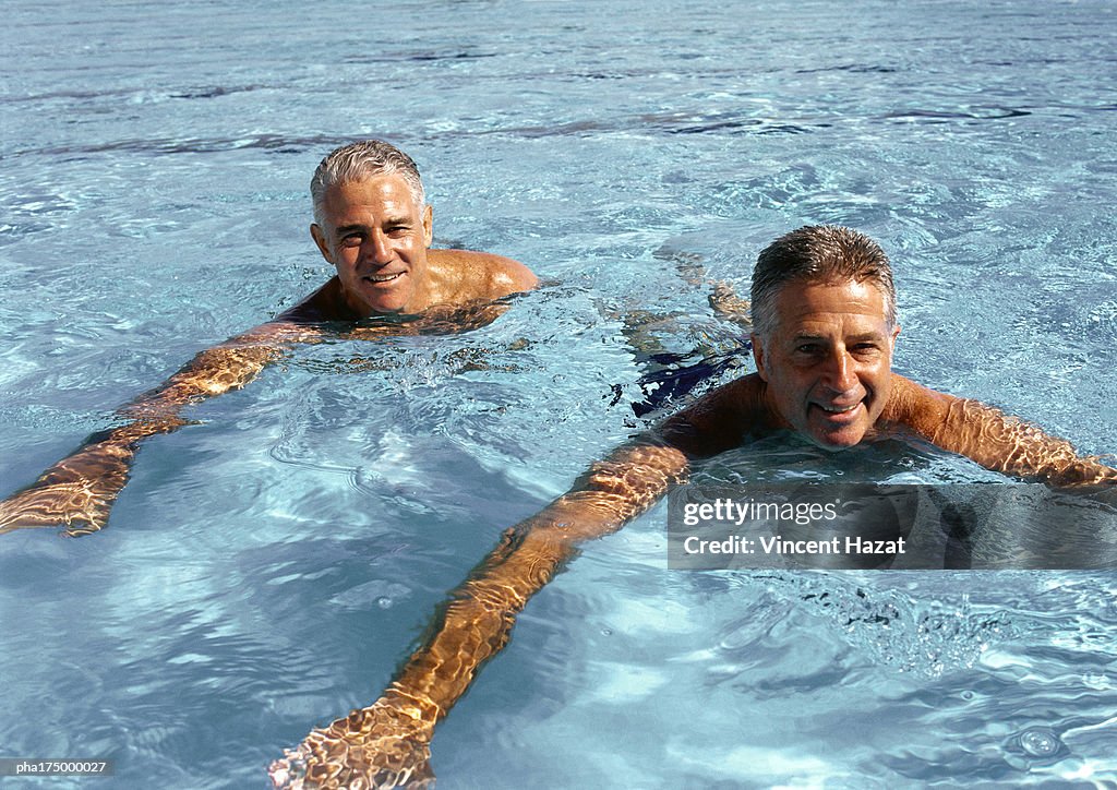 Two mature men in swimming pool, smiling