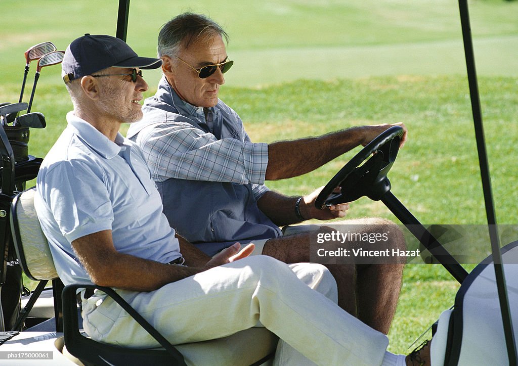 Two mature golfers in golf cart, close-up, side view