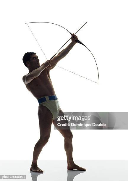 half-nude man bending bow, side view - arco y flecha fotografías e imágenes de stock