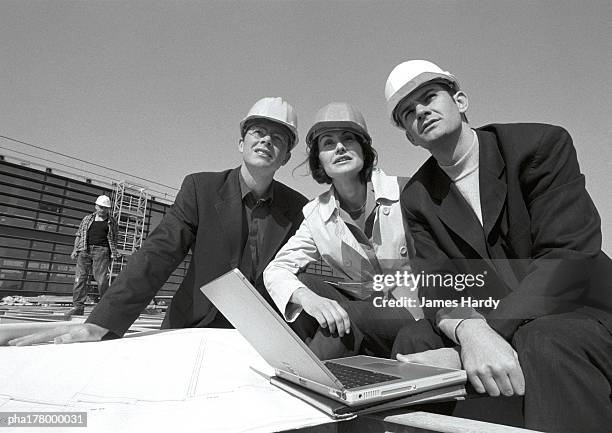 three people wearing hard hats,  laptop computer, b&w - being watched stockfoto's en -beelden