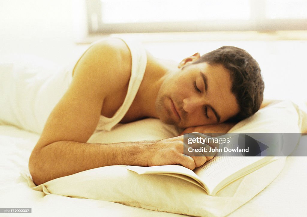 Man lying down in bed with hand on book