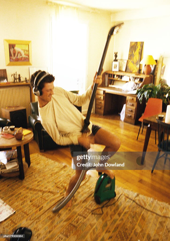 Man with headphones, holding vacuum cleaner, pretending to play guitar