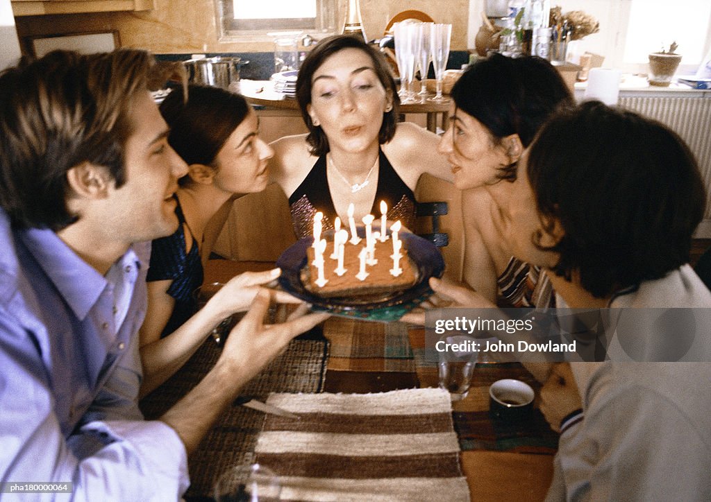 Four people holding cake, woman blowing candles