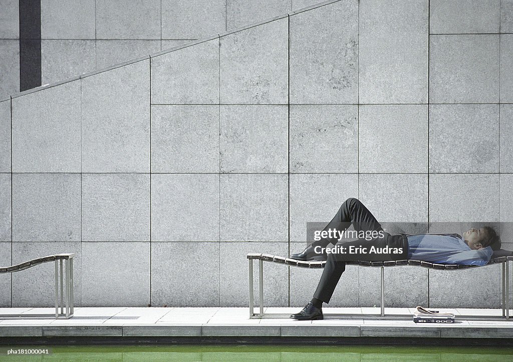 Businessman lying on bench outdoors