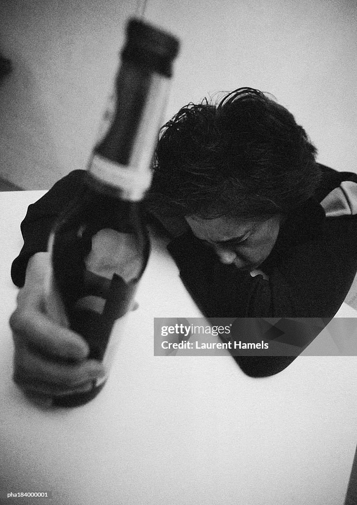 Woman holding bottle, leaning head on table, b&w