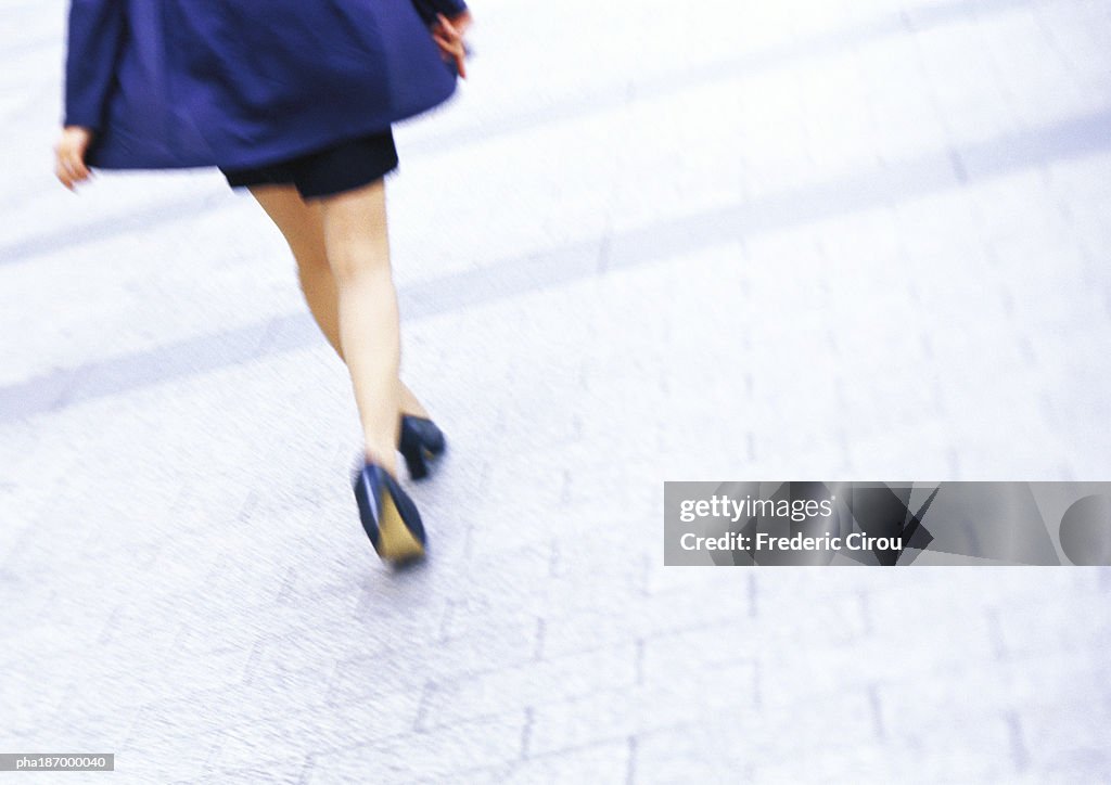 Businesswoman walking, low section, tilt, blurred motion
