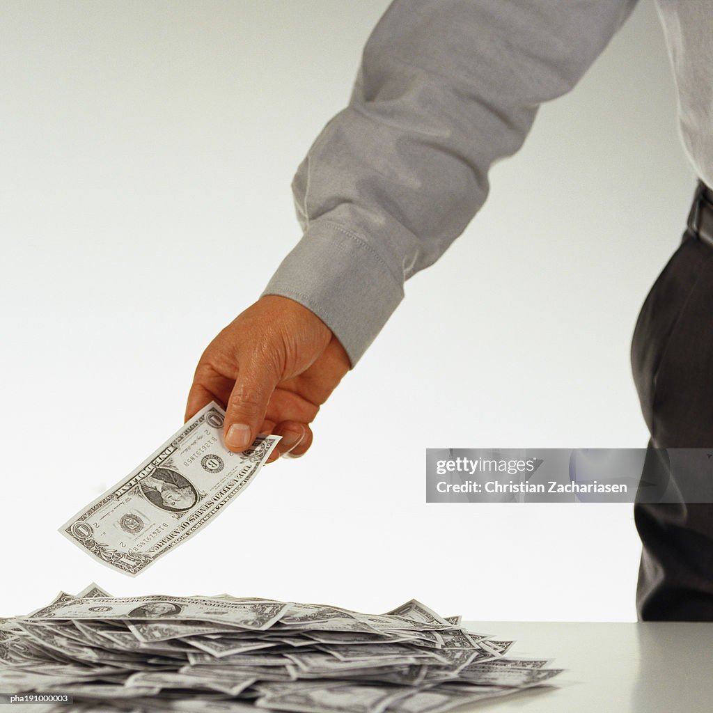 Man holding a dollar over a pile of money.