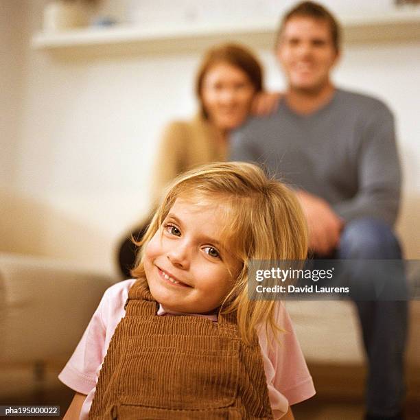 little girl smiling at camera, parents behind her. - laurens foto e immagini stock