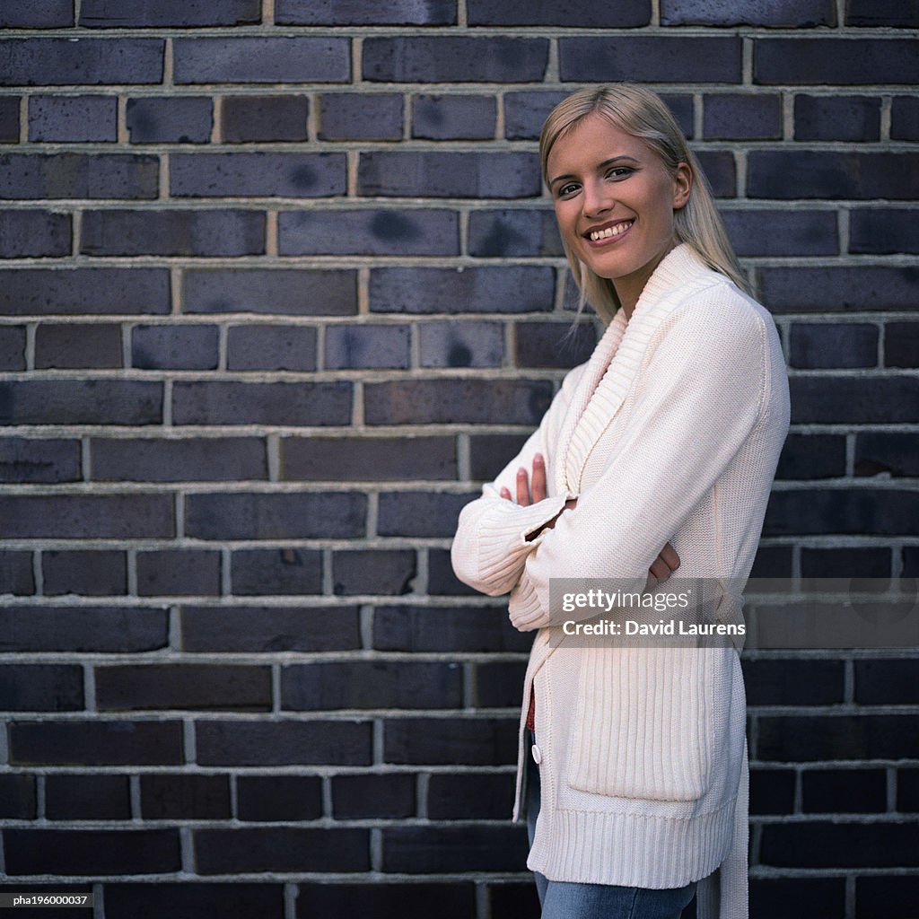 Woman smiling at camera, standing next to brick wall.