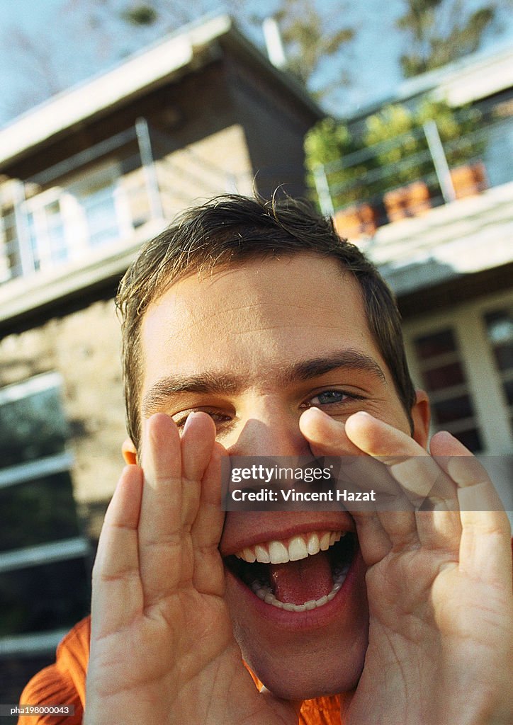 Man's hands around open mouth, close-up, house in background