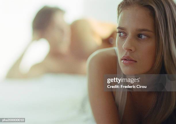 close up of woman, man blurred in background, laying in bed. - betrayal photos et images de collection