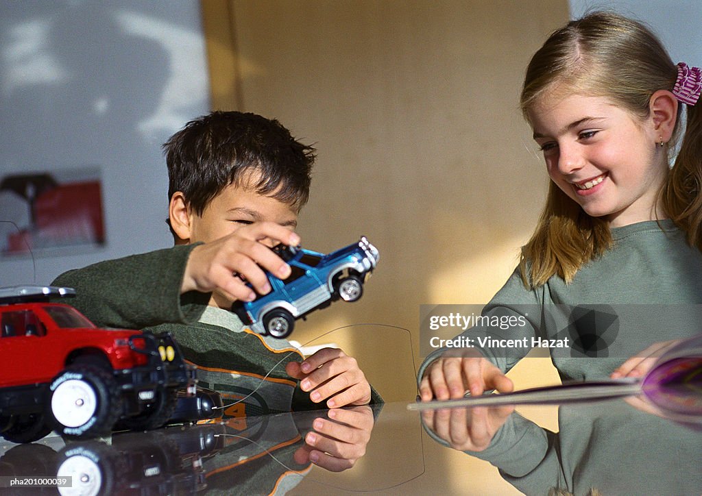 Boy and girl playing together at table with toy cars.