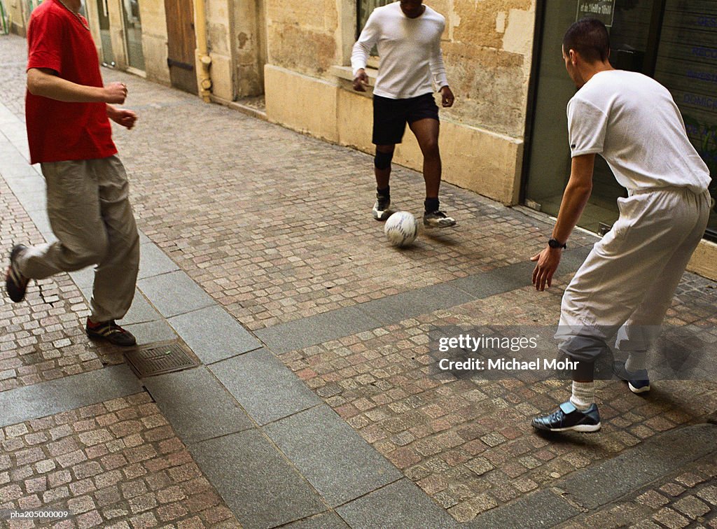 Men kicking soccer ball in street