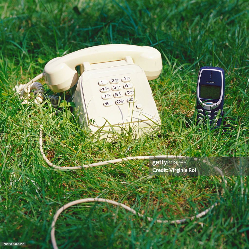 Telephone and cell phone on grass.