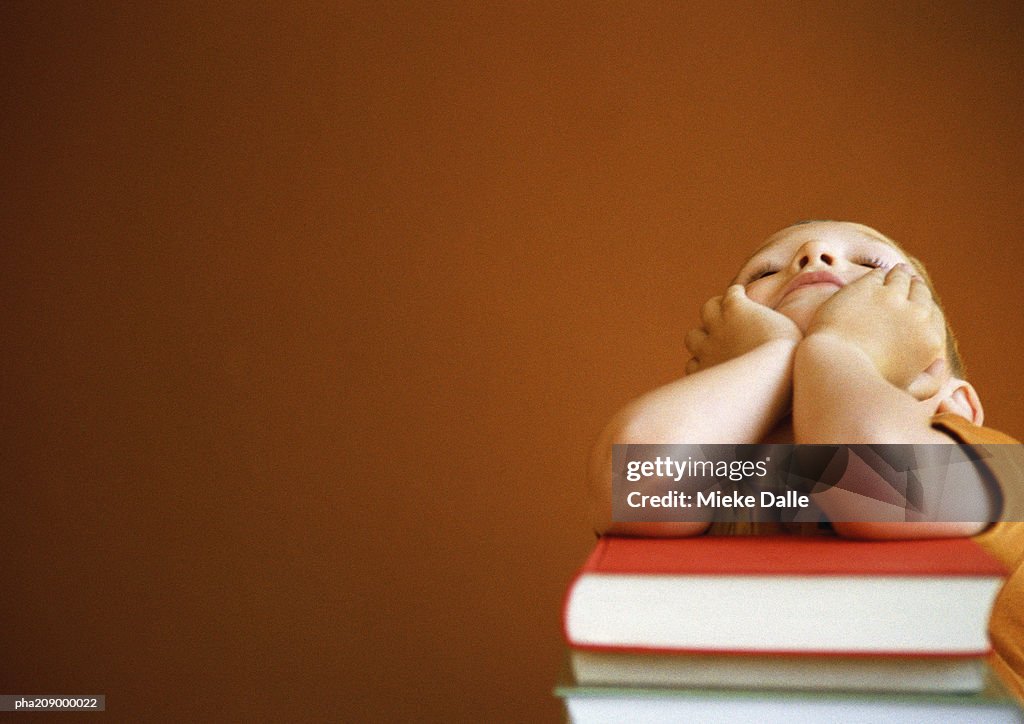 Child leaning on books, head in hands, portrait.