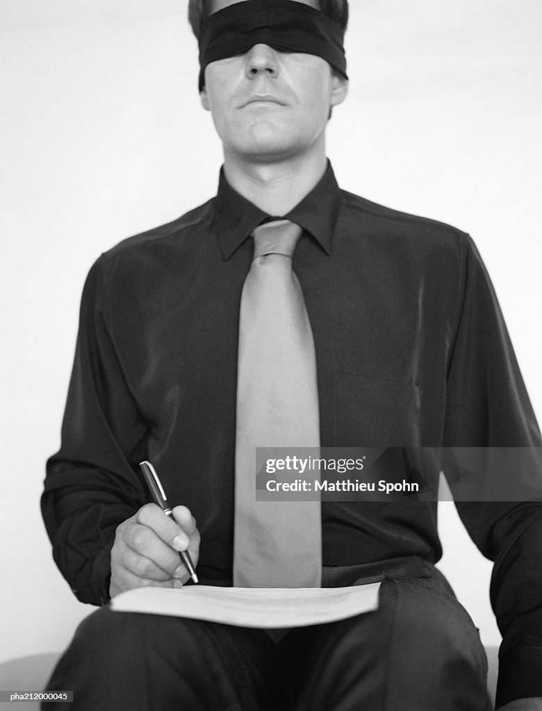 Man wearing blindfold, writing in a book, b&w.
