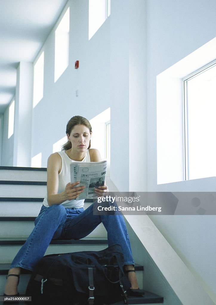 Woman sitting on stairs, reading newspaper, full length