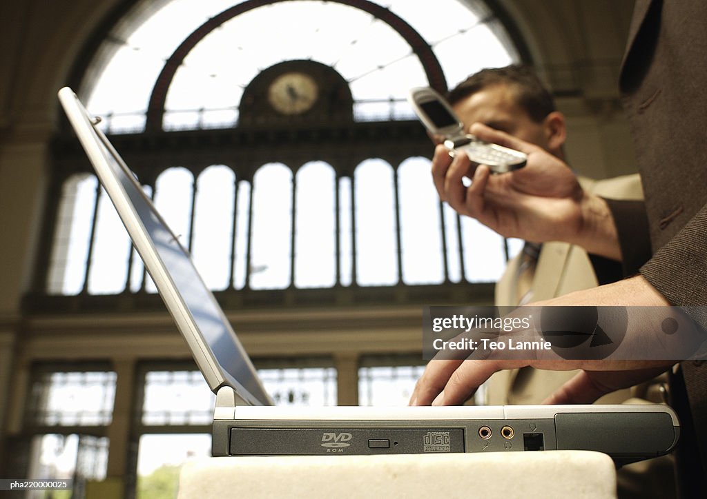 Two businessmen using laptop and cell phone, side view.