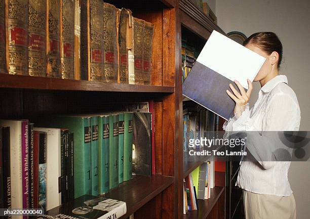 young woman taking book from bookshelf. - viso nascosto foto e immagini stock