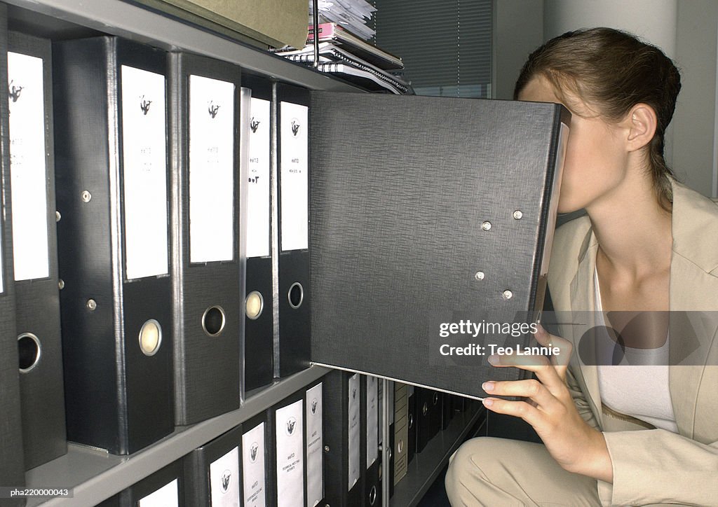 Young businesswoman, taking file from shelf.