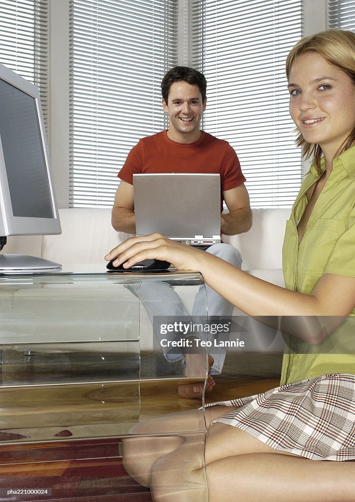 Woman kneeling on floor, holding computer mouse, side view, man using laptop computer in background
