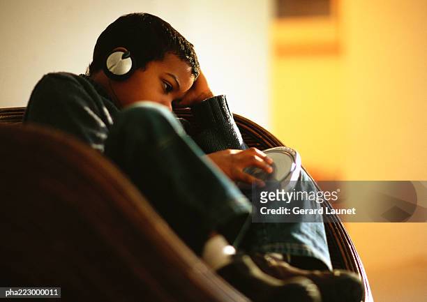 young boy sitting in chair listening to music through headphones. - kids rom stock pictures, royalty-free photos & images
