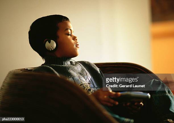 young boy sitting in chair listening to music through headphones with eyes closed. - escape rom stock pictures, royalty-free photos & images