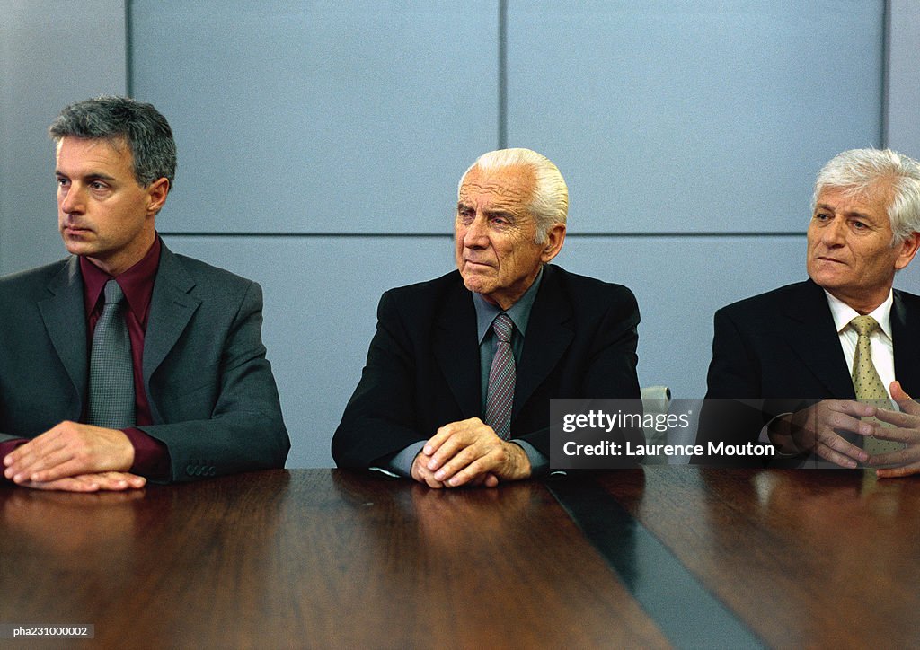 Three businessmen sitting at conference table with hands on table, portrait