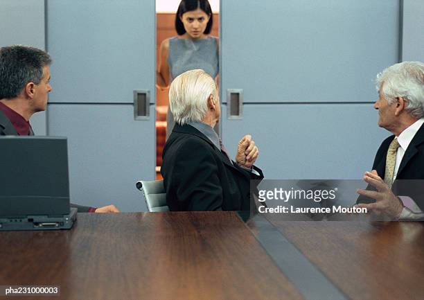 three businessmen sitting at conference table,  businesswoman entering door, portrait - door stockfoto's en -beelden