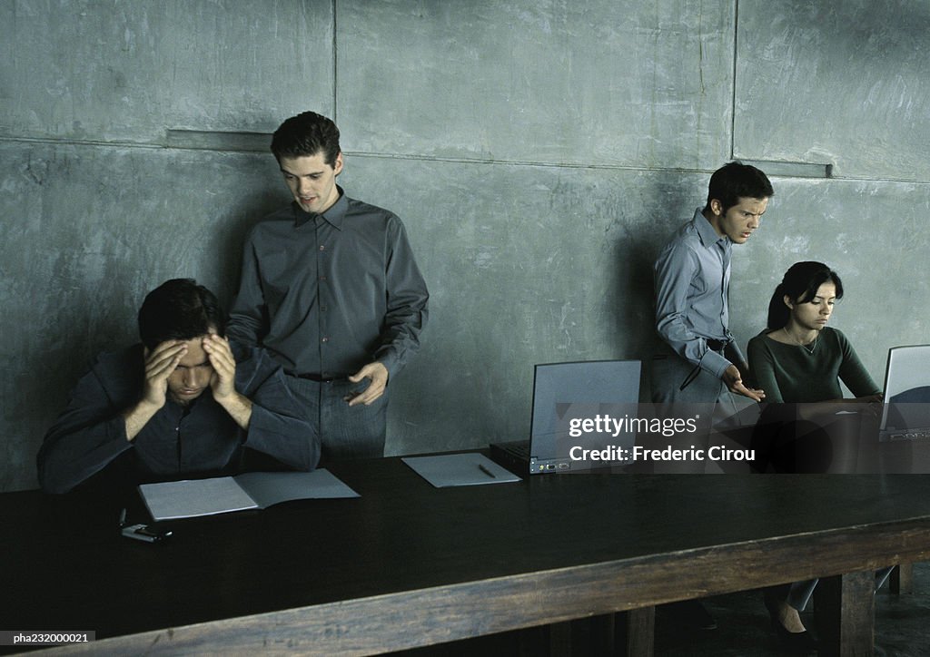 Two men standing helping man and woman sitting at table.