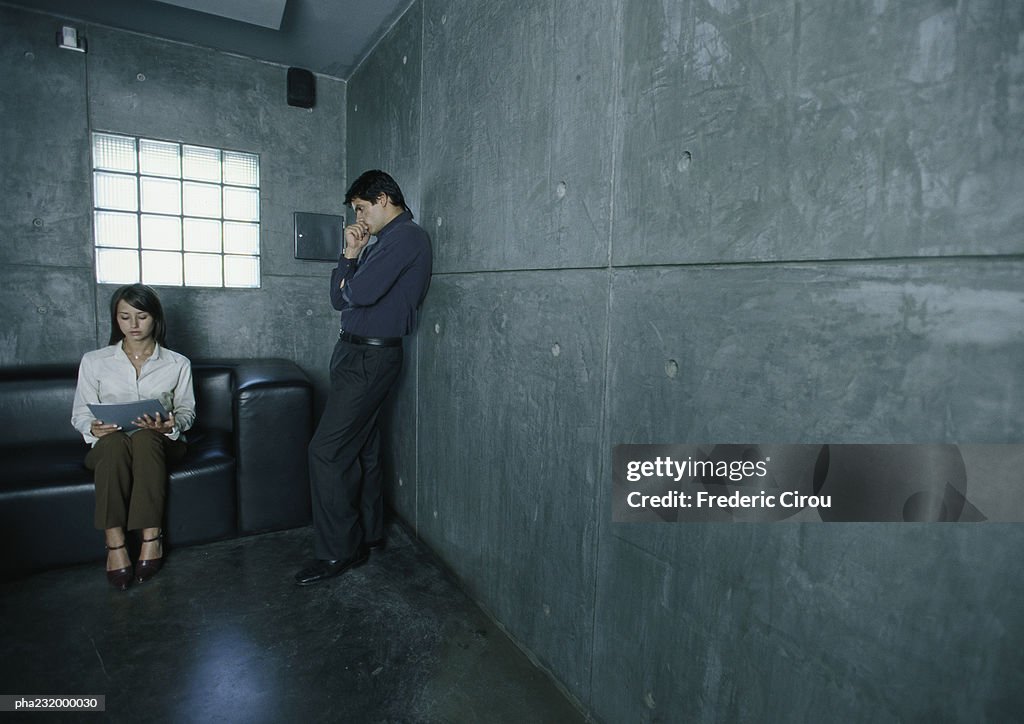 Man standing next to woman sitting on couch looking at paper.