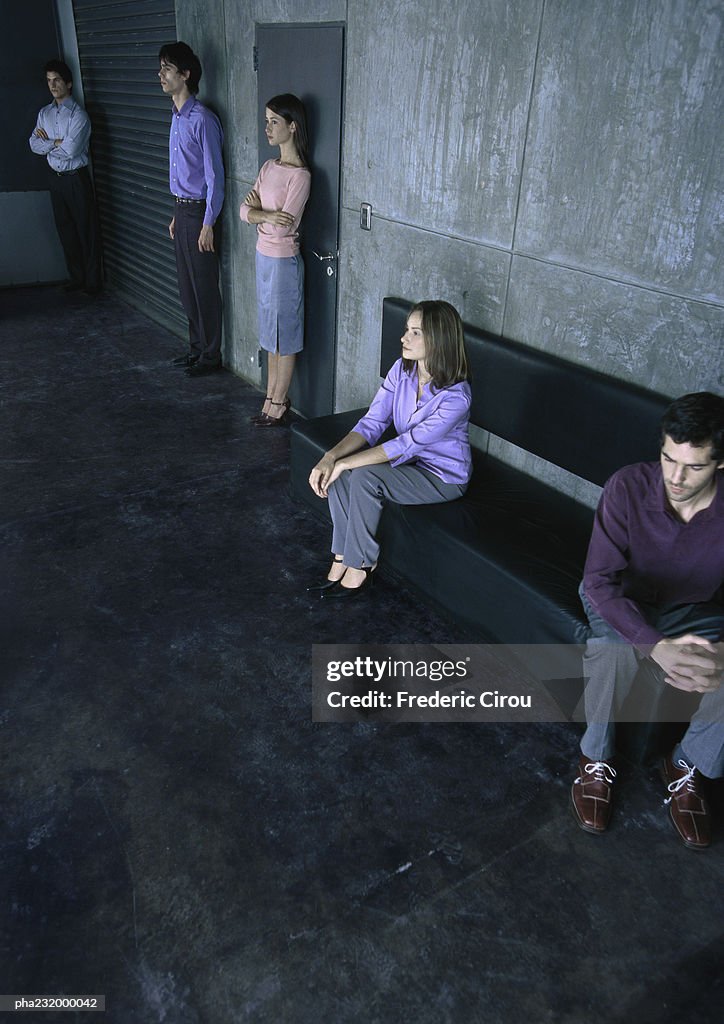 Two people sitting on bench, three people standing, all spaced apart from one another.