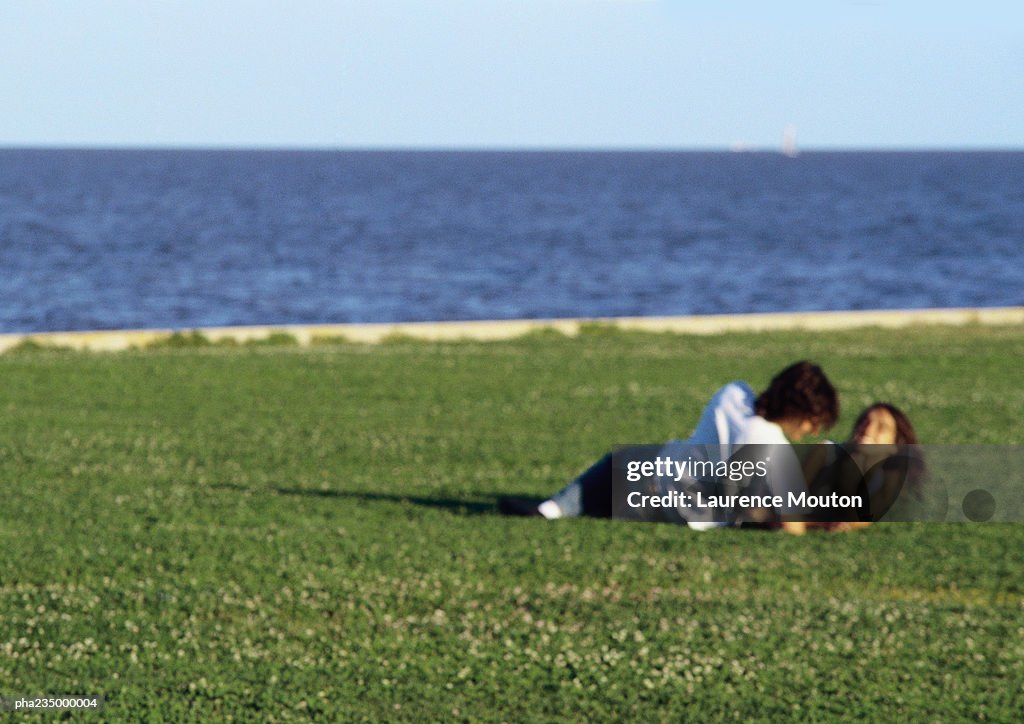 Man and women laying together on grass by the water, blurred.