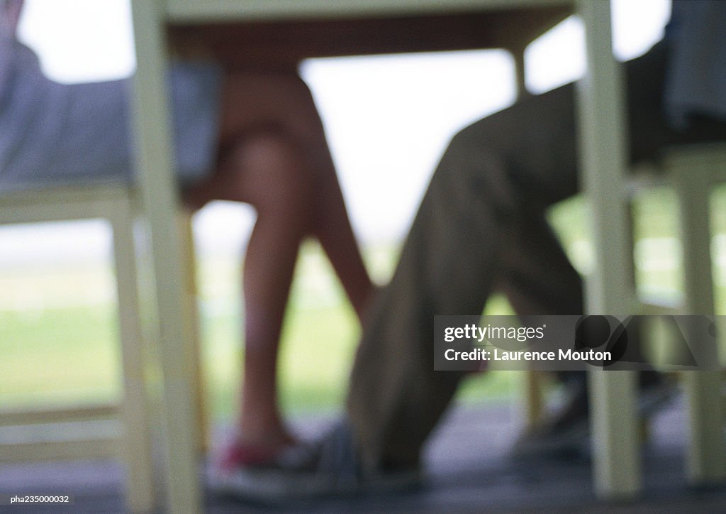 Man and woman sitting at table, silhouette blurred,  focus on feet.