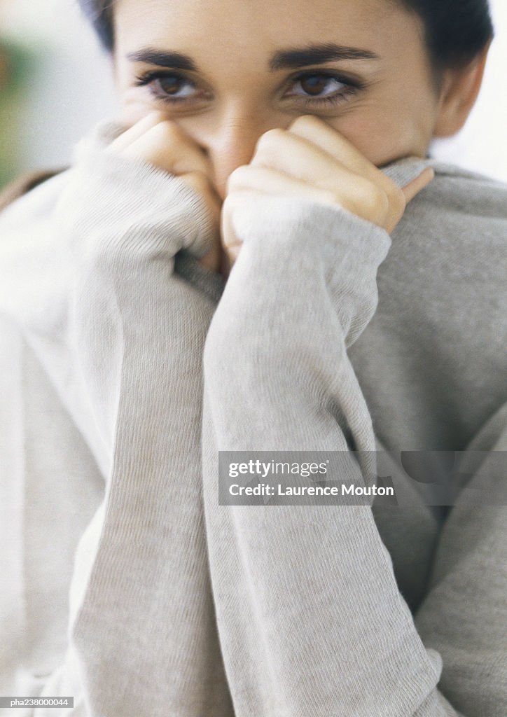 Woman holding on to ends of sleeves, covering lower part of face, head and shoulders, parital view, close-up