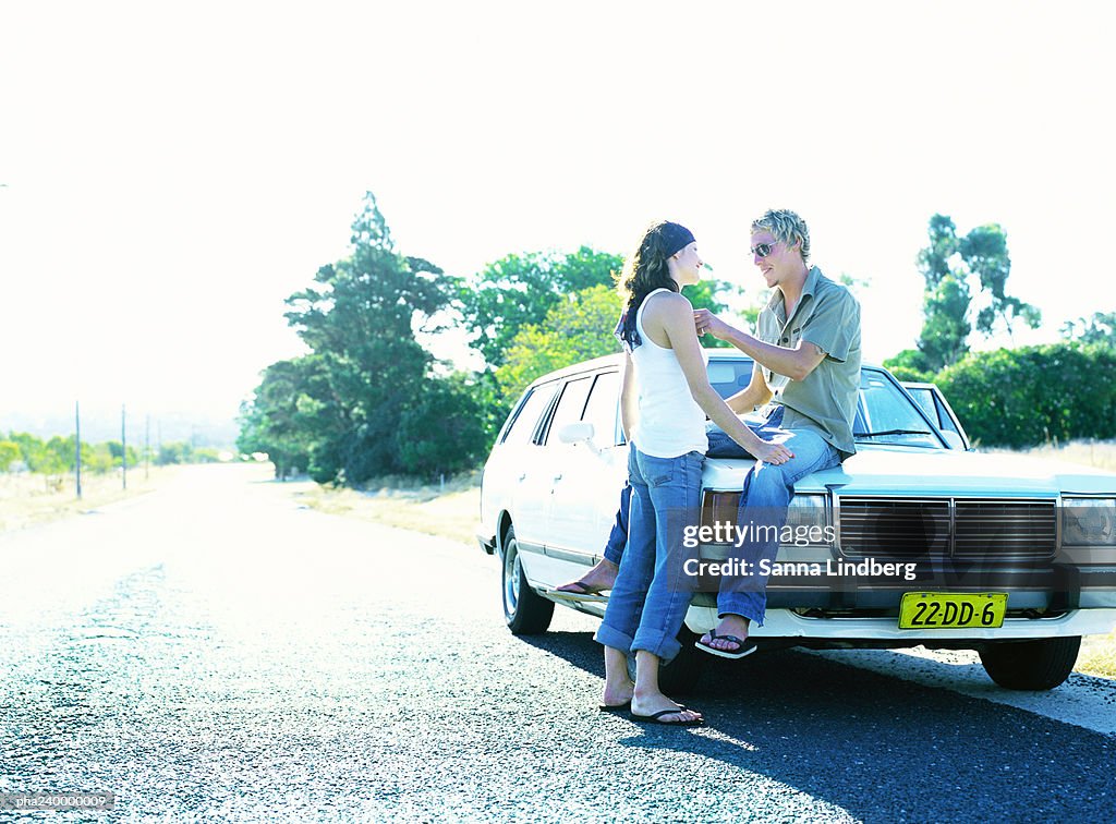 Woman in front of man sitting on car hood